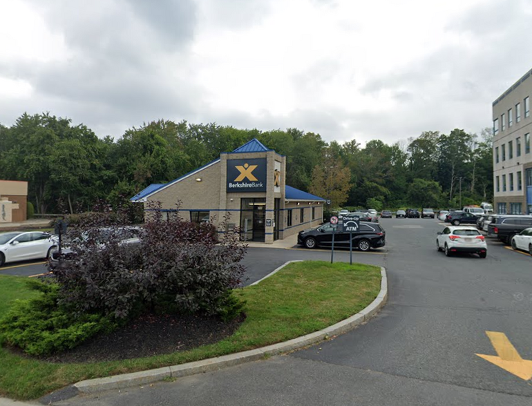 A one-story bank building sits behind a parking lot and grassy medain