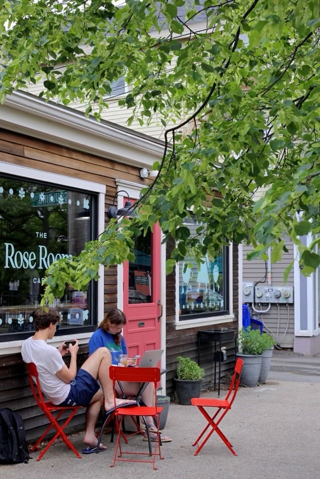 Two people sit on red chairs looking at their phones outside of a coffee shop.