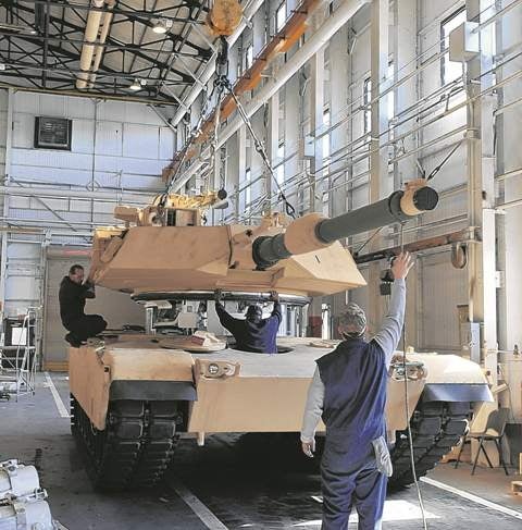 Turret of a tank being installed by three workers