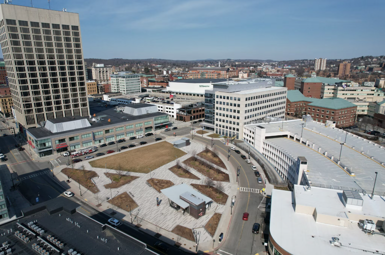 An open space with grass and paved walkways surrounded by buildings in a mid-sized city
