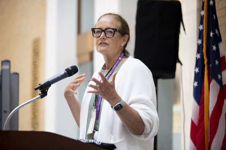 Woman in white sweater at podium speaking