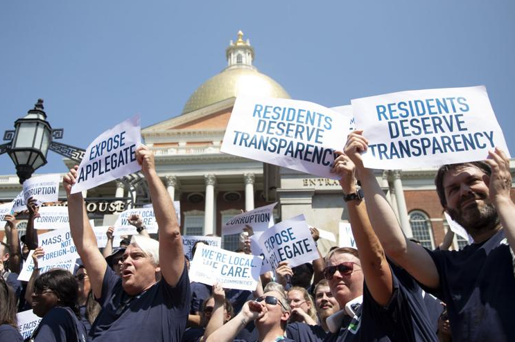Group of people stand outside the statehouse with protest signs 