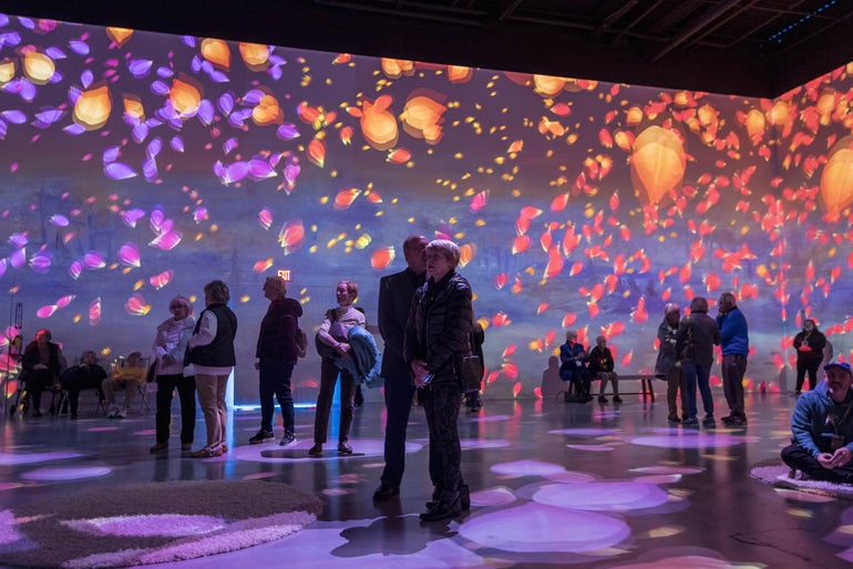 People standing in an immersive experience where a Claude Monet painting is projected in 3D on the walls of a room
