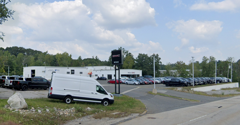 An auto dealership with a van parked in front and a number of cars parked behind it