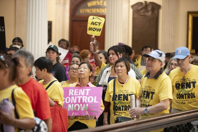 Group of people rallying in the state house holding signs and wearing shirts advocating for rent control
