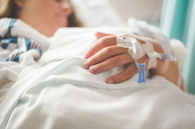 Woman lies in hospital bed with tubing attached to hand