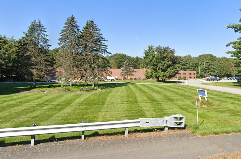 A large lawn with a two-story brick industrial building and trees behind it