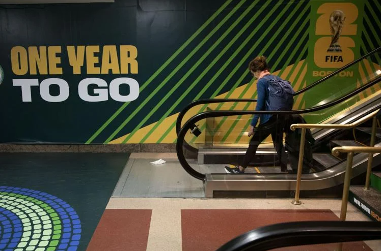 A person exits an escalator in front of an ad for the 2026 FIFA World Cup. 