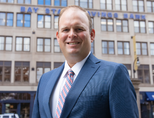 A man wears a blue suit and a pink & blue tie