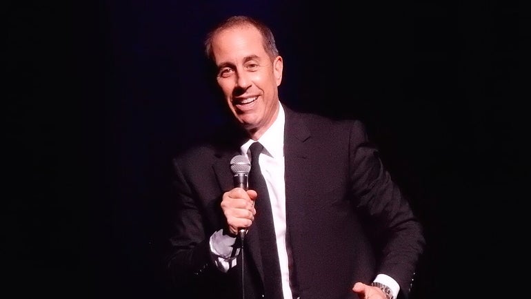 A man in a suit holds a microphone while smiling