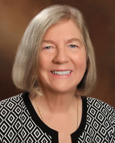 A woman with chin-length grey hair wears a black and white top.