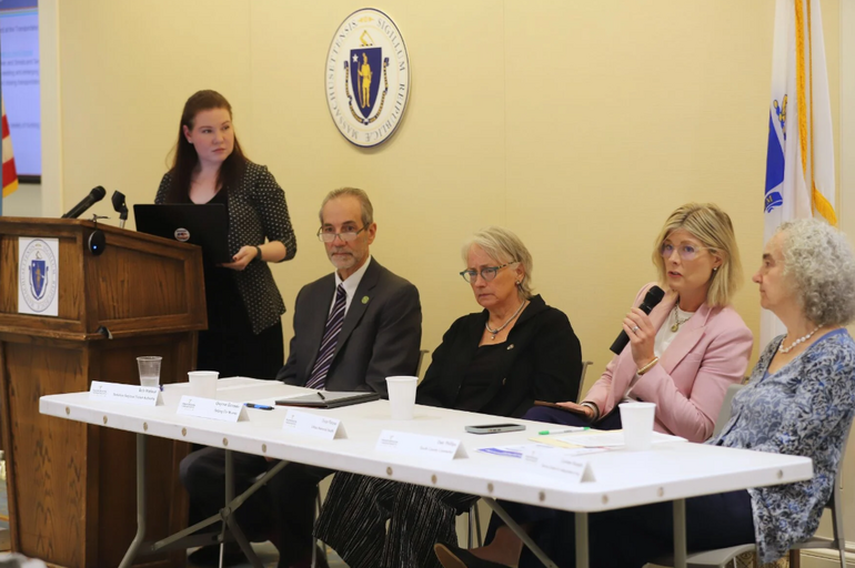 One person at a podium and four people at a table participate in a roundtable discussion.