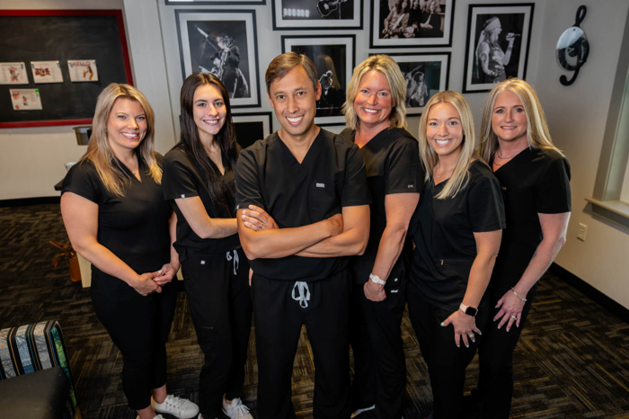 A groupe of one man and five women stand in black scrubs in a medical office. 