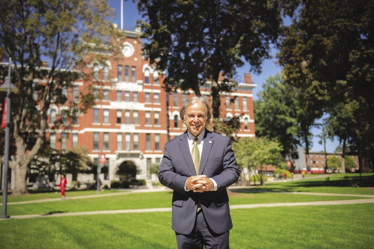 Man in suit stand on college quad in front of a large brick academic building