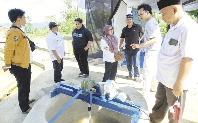 A group of people stand around a small hydroelectric power plant in Indonesia.