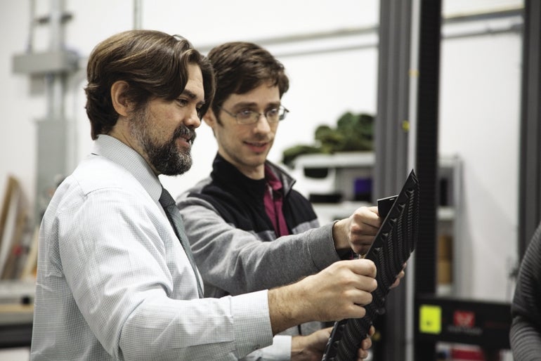 Two Multiscale Systems employees are pictured in a workshop looking at a black composite.