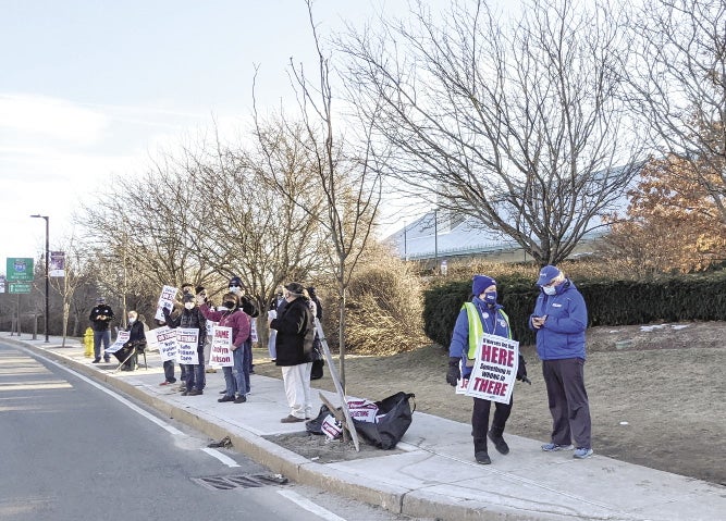 A picket line of union workers stand on the sidewalk in front of a hosiptal.
