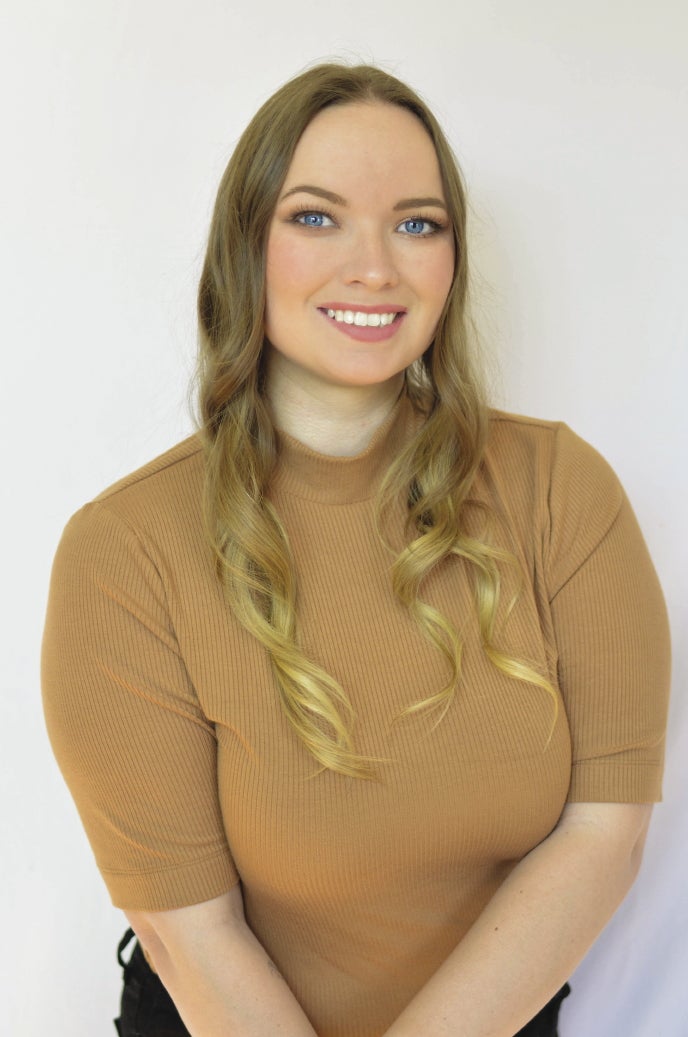 A headshot of a woman with long blonde hair and a tan mock neck knit top