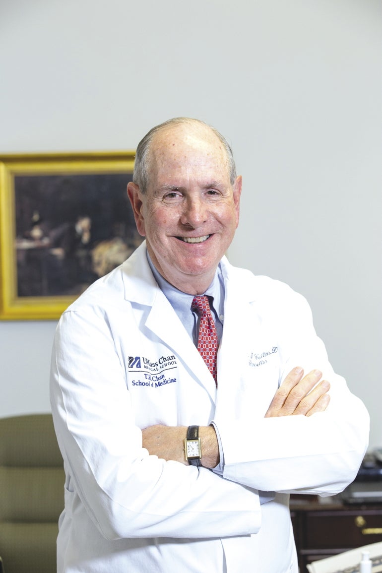 A man in a white lab coat stands with crossed arms and smiles for the camera