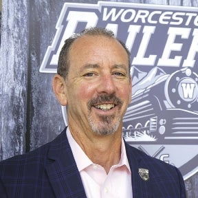 A man with a beard in a dark navy suit jacket and light pink shirt 