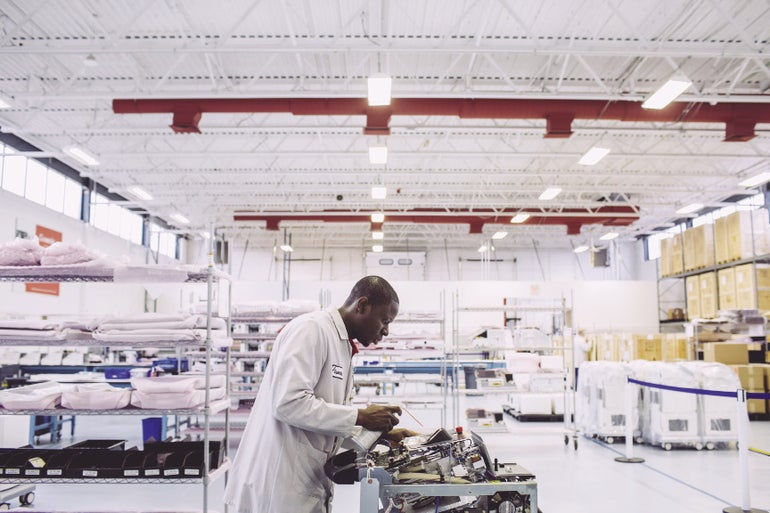 A man in a lab coat cleans a piece of machinery in an industrial building