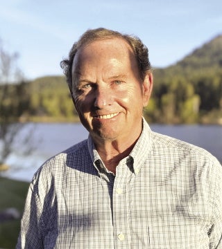 Man in checkered dress shirt stands in front of river