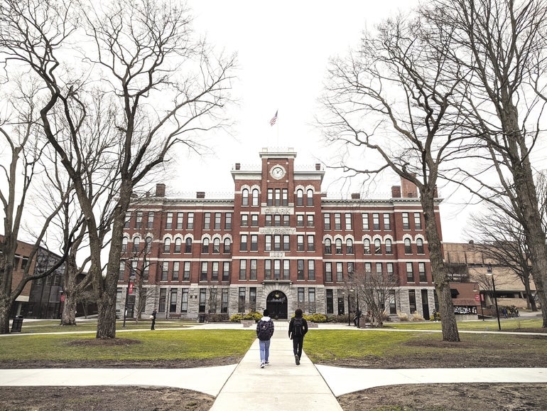 Two people with backpacks walk towards a large brick school building