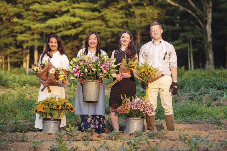 Three women and a man stand in a farm's field holding flowers