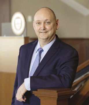 A man wearing a blue suit and blue tie stands at the bottom of a staircase.