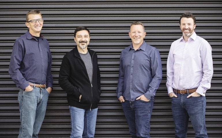 Four men stand in front of a currugated steel door