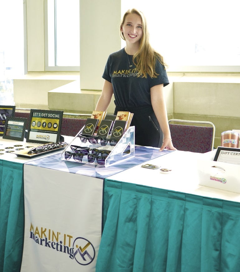 A woman stands in front of a table with a green skirt.