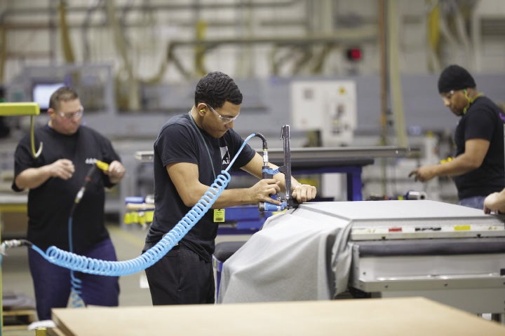 Three people in a factory, with one person operating a air-powered tool.