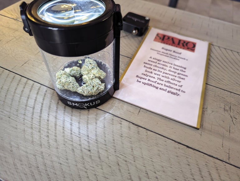 cannabis buds sit in a clear jar next to a label describing the product