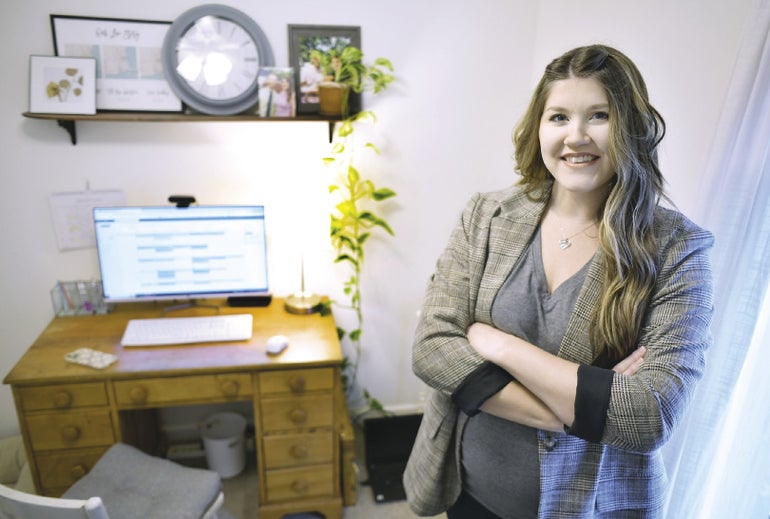 A woman in a gray suit stands in front of her work-from-home station