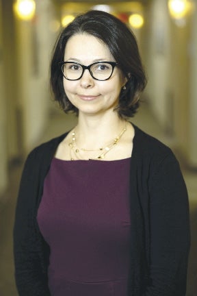 A woman with short, straight black hair wears a black cardigan and dark purple top.