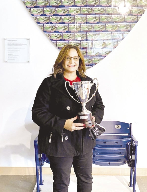 A woman in a black jacket and red shirt holds a trophy.