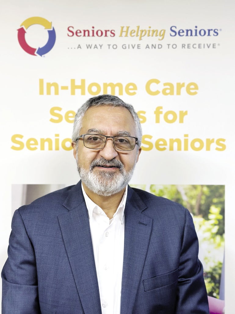 A man with white hair and beard wears glasses and a blue suit jacket.