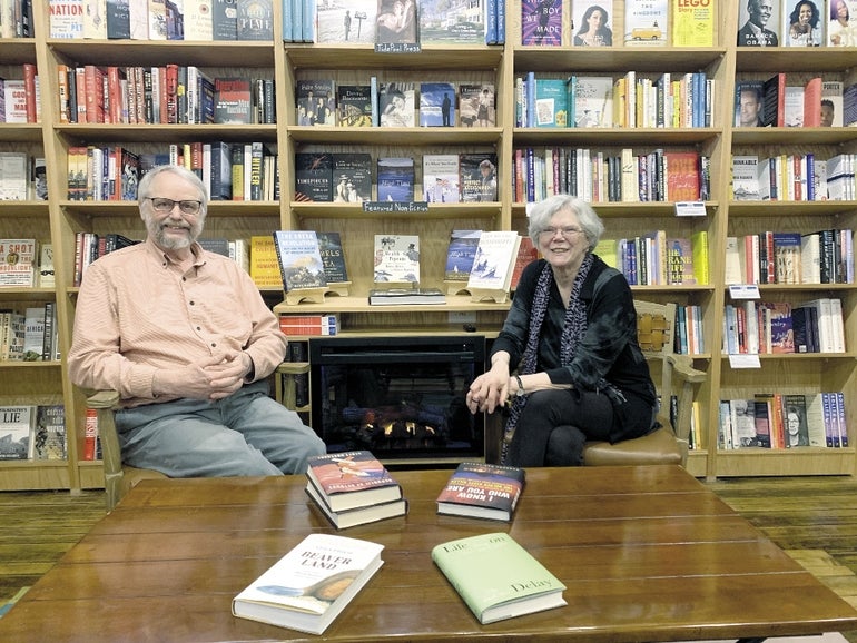 Tidepool Bookshop owners Jo and Huck Truesdell sit in front of a fireplace and shelves of nonfiction books.  