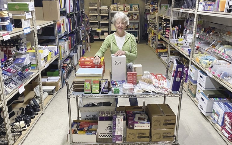 A woman stands in a warehouse surrounded by office supplies.