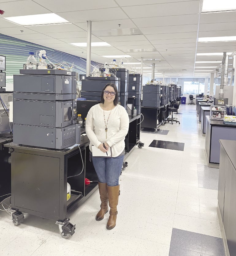 A woman stands in front of lab equpiment