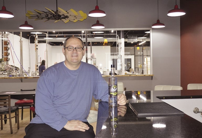 Barry Bacon, owner of Spicy Water Distillery in downtown Millbury, sits at the distillery's bar.