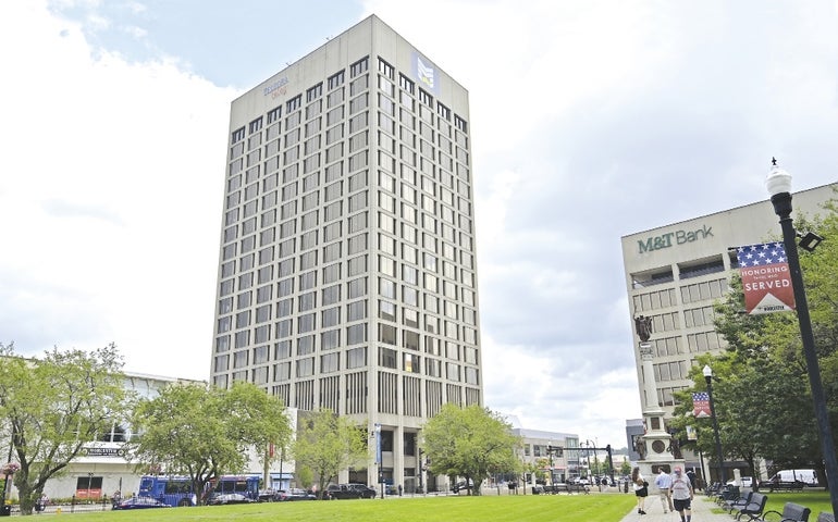 A concrete office tower beyond a field of green grass. One half of a sign that once read Telegram and Gazette is visible atop the building