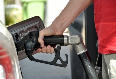 A photo of someone in a red shirt using a gasoline pump.