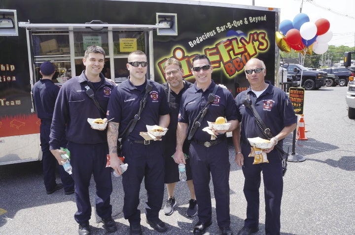 Five men stand smiling in front of a BBQ catering truck