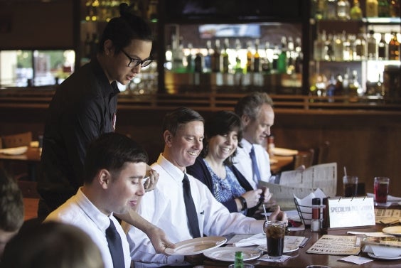 A waiter puts a plate down in front of four people sitting at a restaurant table