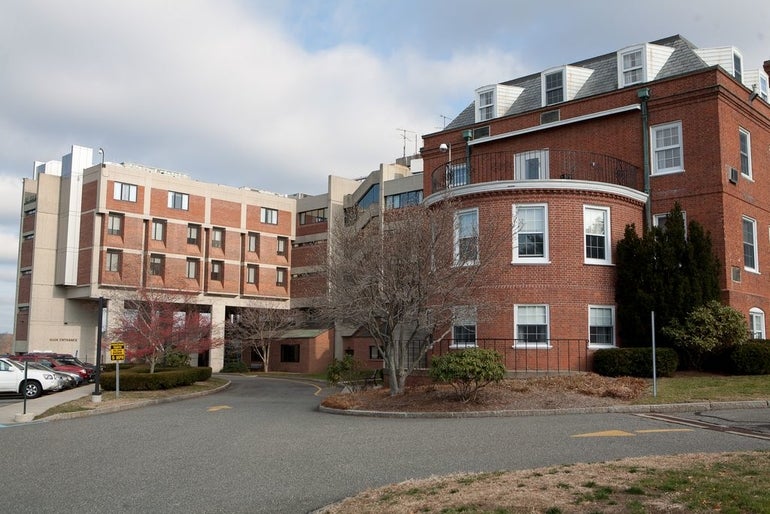 A brick hospital building sits behind a curved driveway with a parking lot on the right.