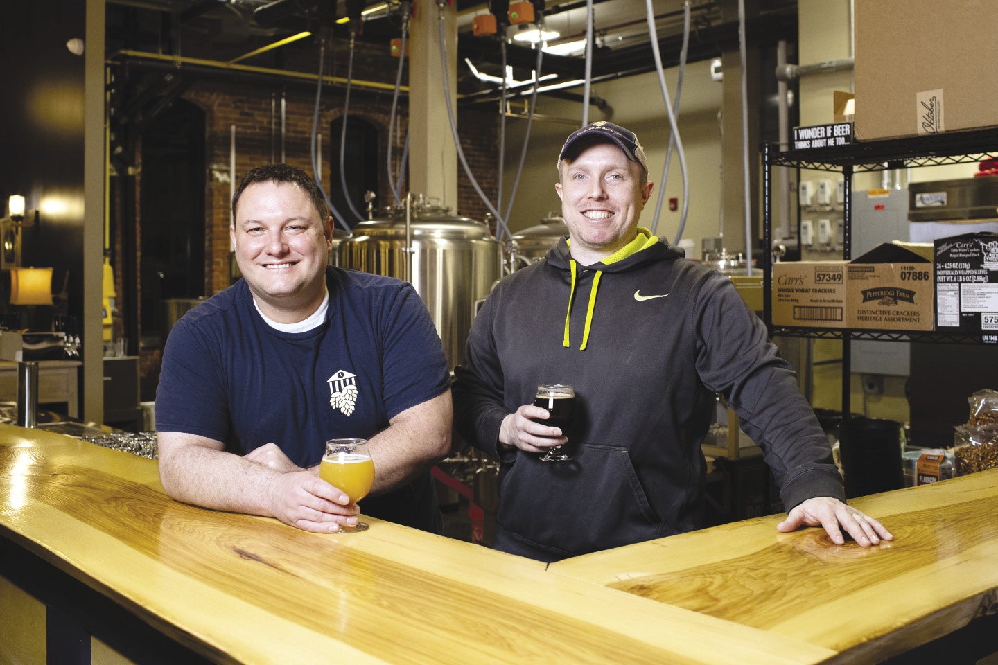 Two people stand behind a bar with beers in their hands