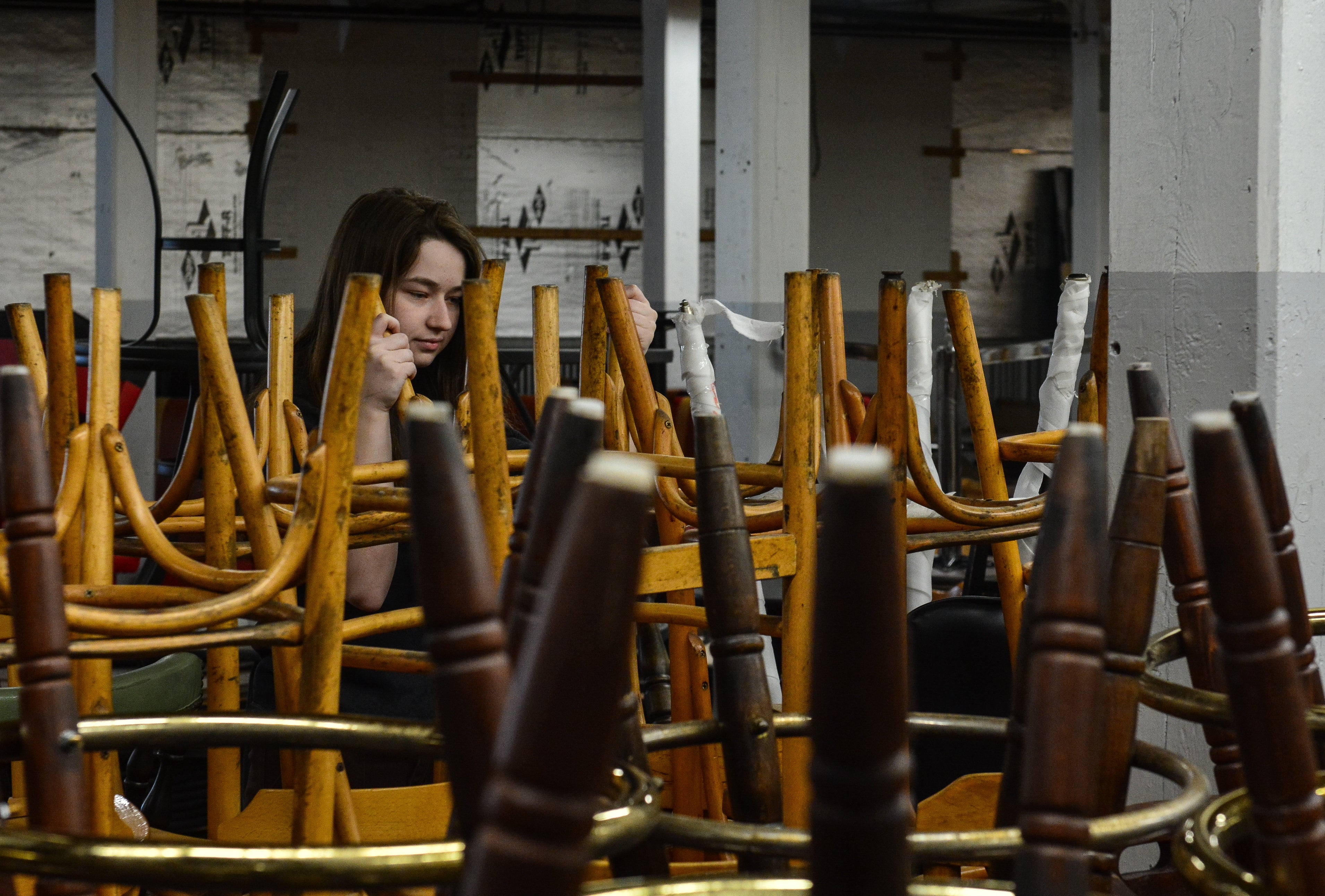 A woman stands among a large group of upside-down chairs