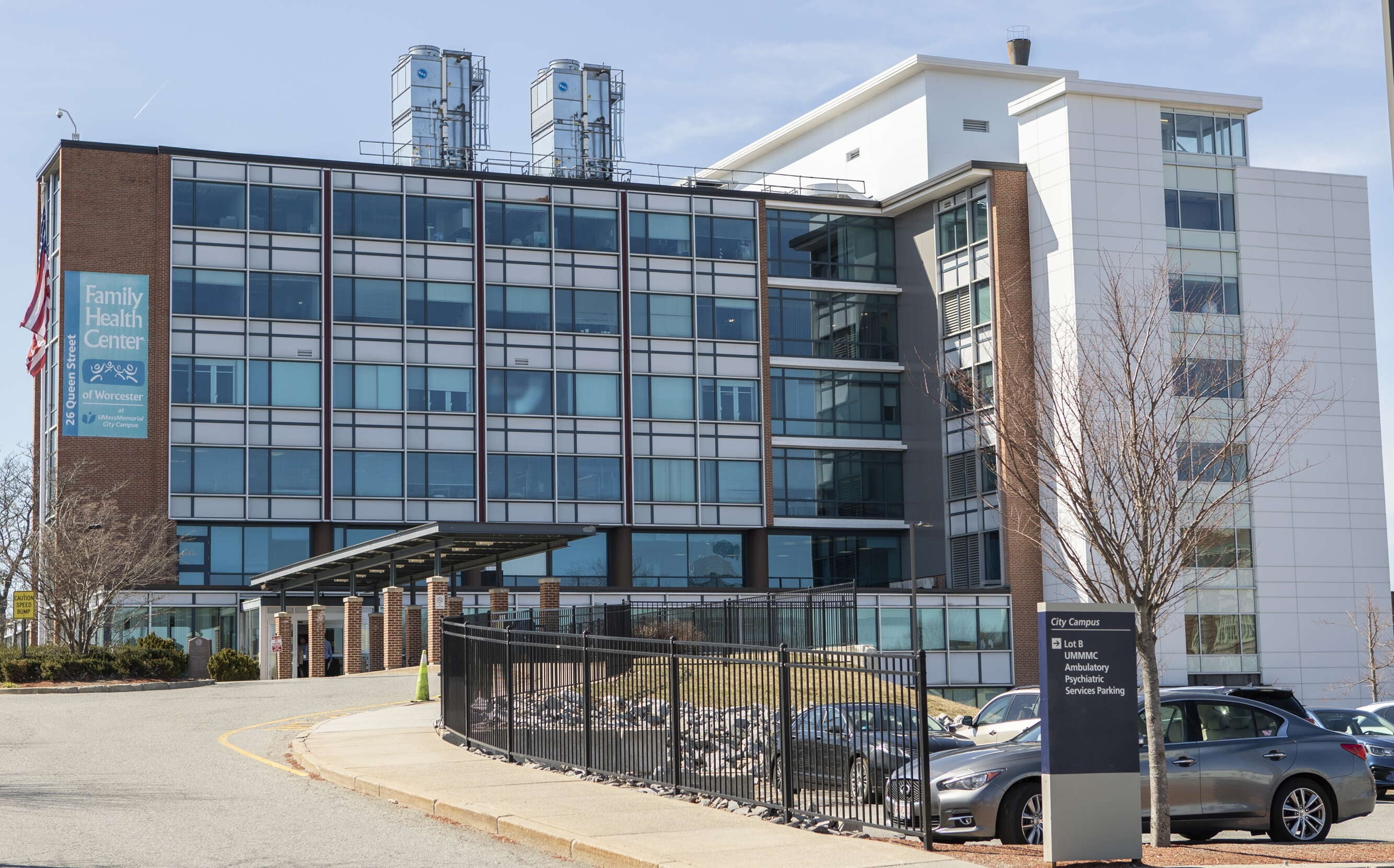 A large building with large windows sits behind a curved driveway leading up to the door and a parking lot to the right.