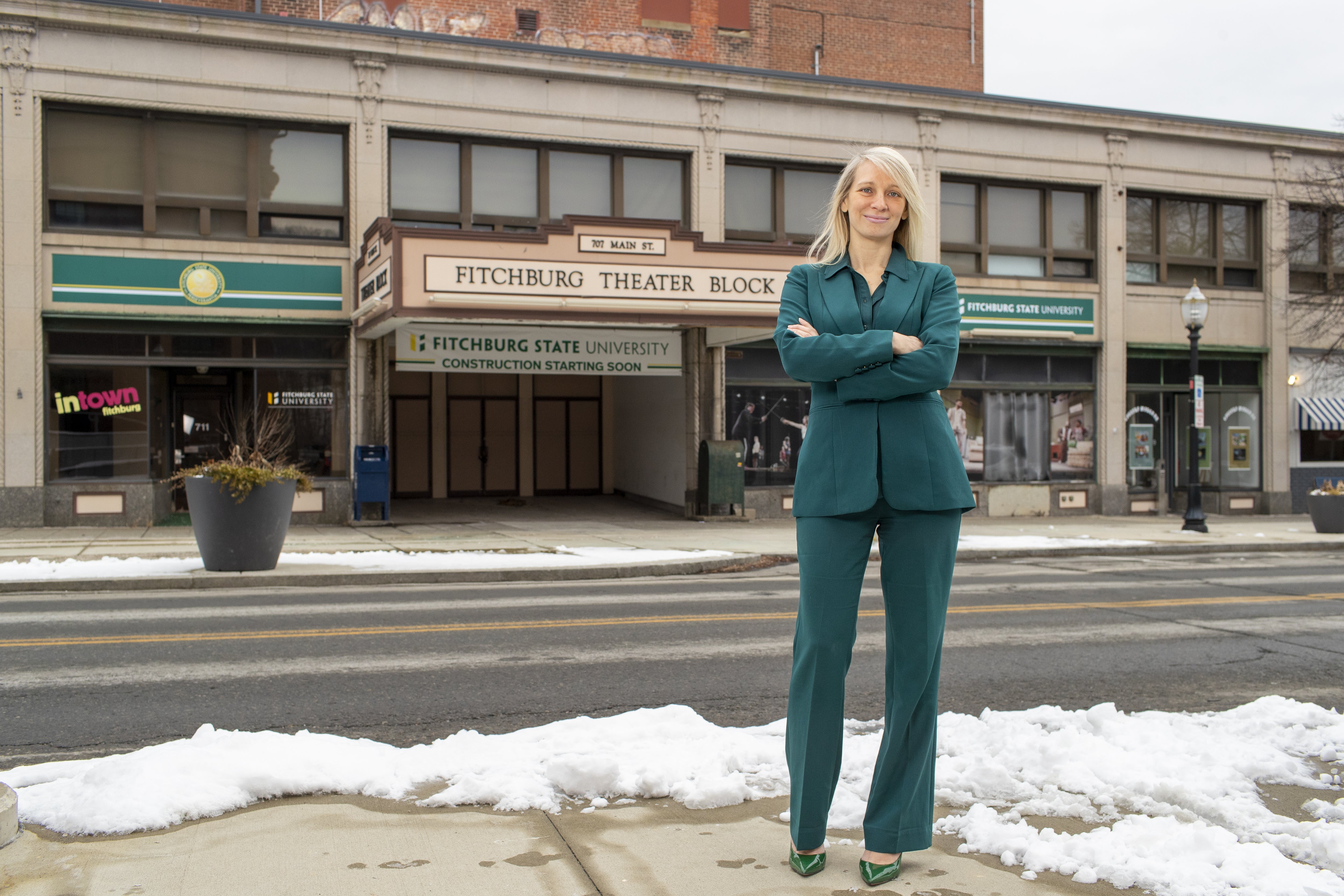 A woman stands in a green suit on a snowy downtown street